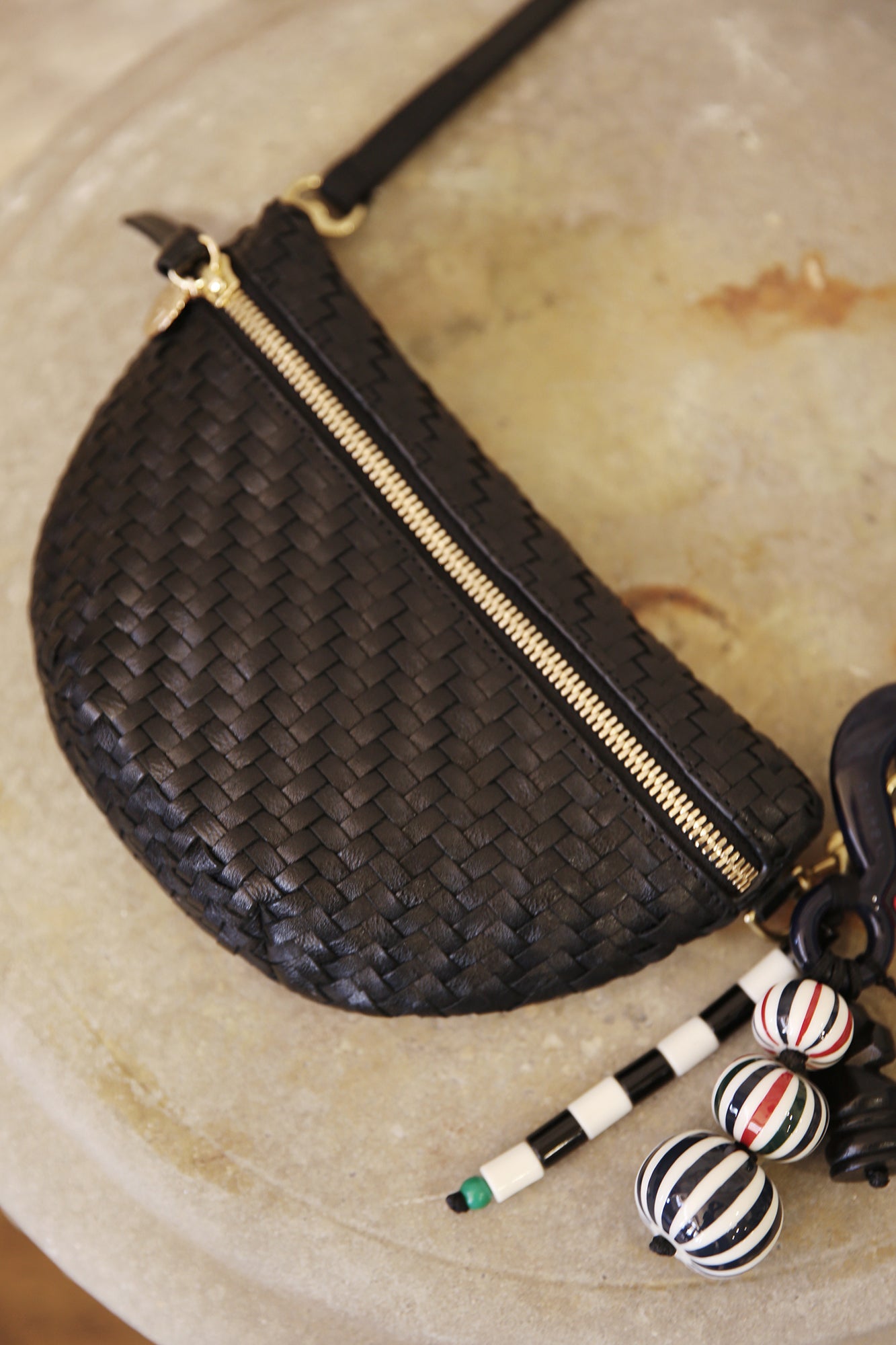 Clare V. Petite Fanny Black woven handbag with gold zipper on a textured surface