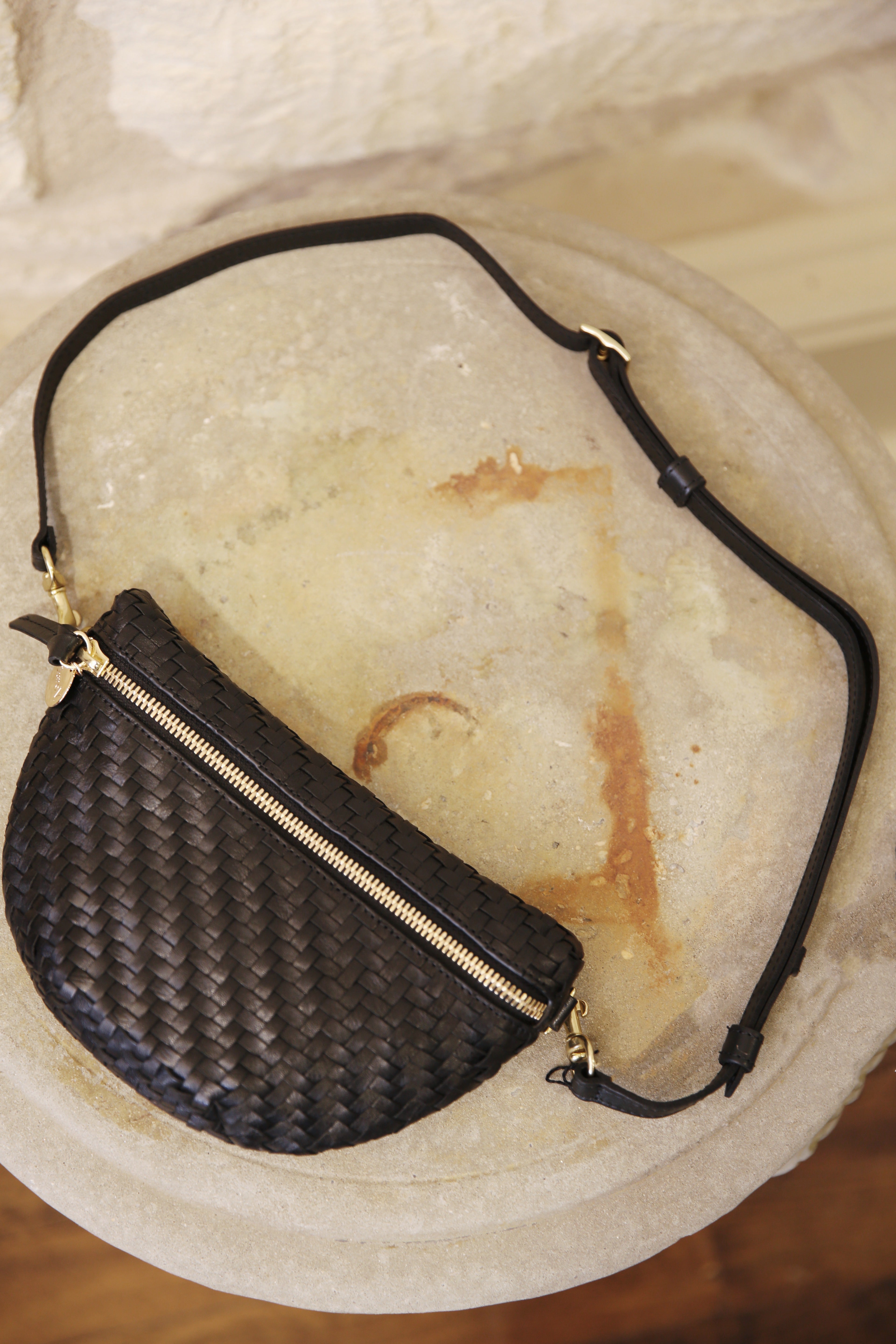 Black woven bag with a gold zipper on a textured surface