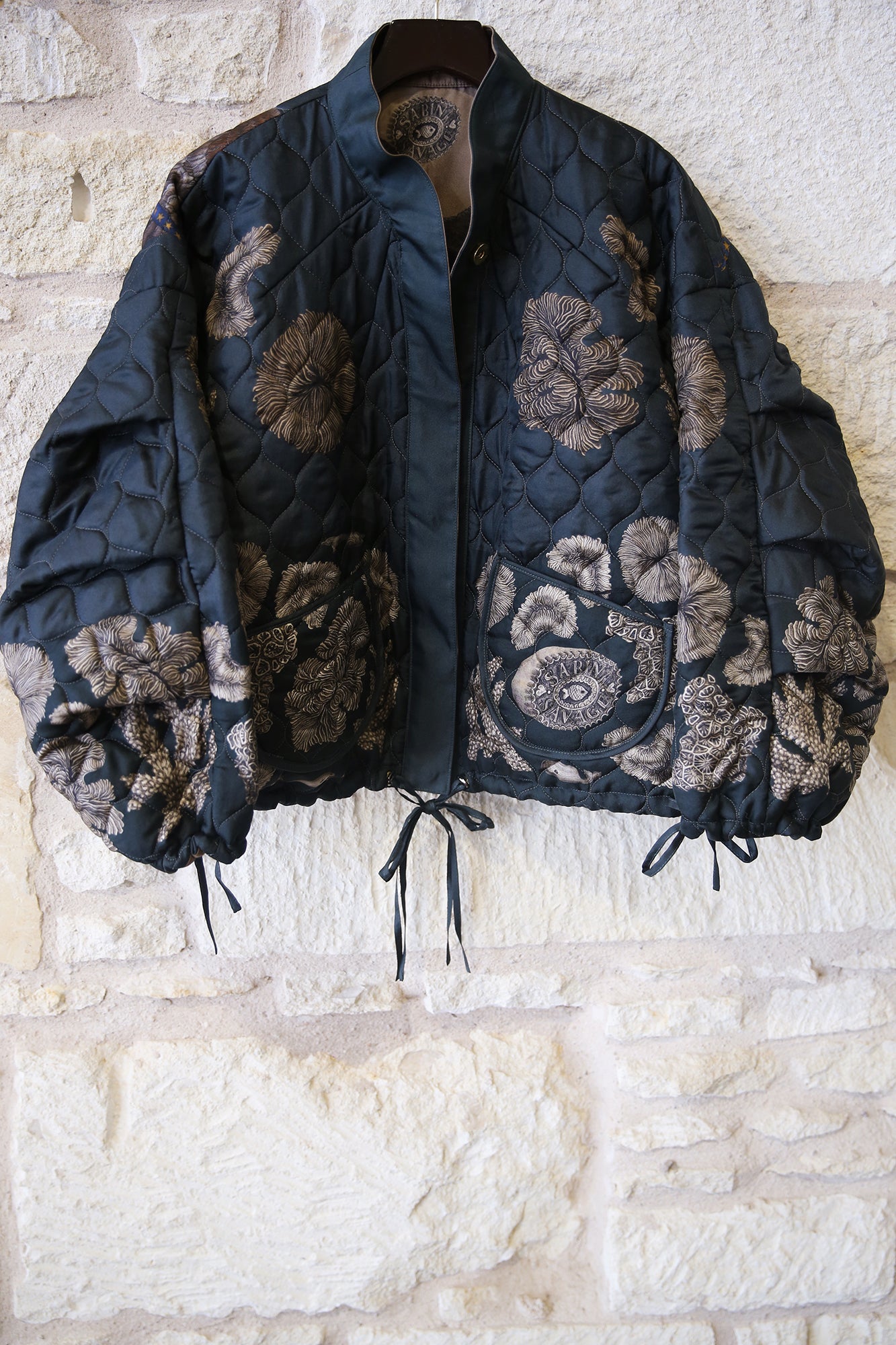 Dark quilted jacket with floral patterns on a stone wall background